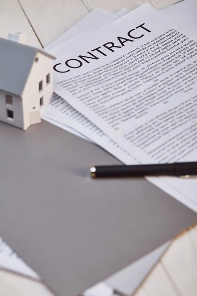 Модель дома на белом деревянном столе рядом с контрактом и ручкой, концепция недвижимости — стоковое фото