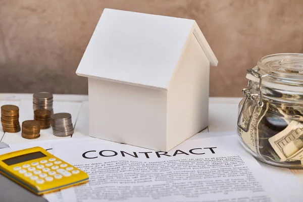 Modelo da casa, moedas, calculadora amarela perto do contrato e da caixa de dinheiro, conceito imobiliário — Fotografia de Stock