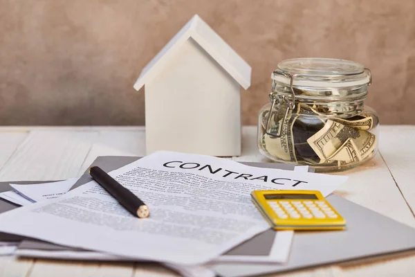 Casa modello su tavolo in legno bianco con contratto, calcolatrice e denaro vicino alla parete martellata marrone, concetto immobiliare — Stock Photo