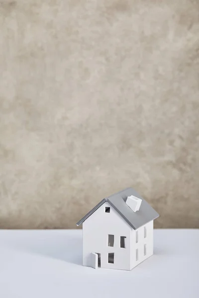 Modelo de casa en mesa blanca cerca de pared texturizada gris, concepto de bienes raíces - foto de stock