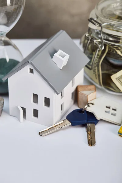 Modelo de casa en mesa blanca con llaves y caja de dinero, concepto de bienes raíces - foto de stock