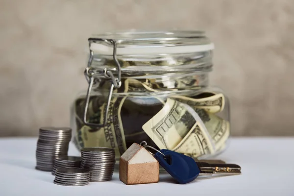 Caja de dinero con billetes de dólar, llaves y monedas en la mesa blanca, concepto de bienes raíces - foto de stock