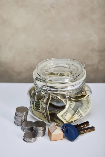 Caja de dinero con billetes de dólar, llaves y monedas de plata en la mesa blanca, concepto de bienes raíces - foto de stock