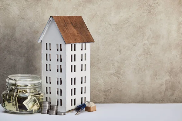 House model, moneybox with dollar banknotes, keys and silver coins on white table on grey background, real estate concept — Stock Photo