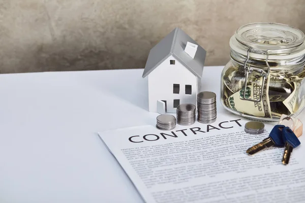 House model on white table with silver coins, keys, contract and moneybox, real estate concept — Stock Photo