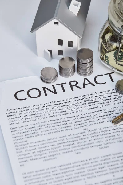 Modelo de casa en mesa blanca con contrato y monedas de plata, concepto de bienes raíces - foto de stock