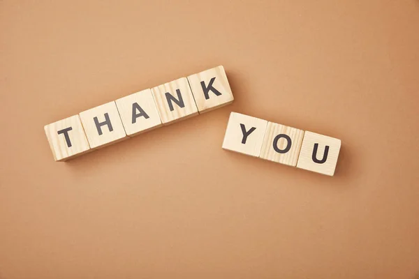 Top view of wooden blocks with thank you lettering on beige background — Stock Photo