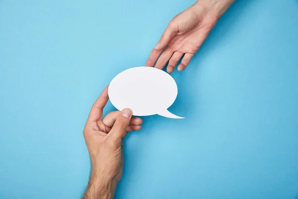 Cropped view of man giving white empty speech bubble to woman on blue background — Stock Photo