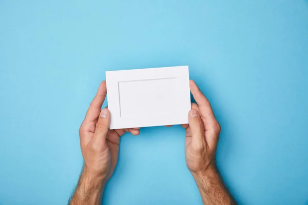 Vista cortada do homem segurando cartão branco vazio no quadro no fundo azul — Fotografia de Stock