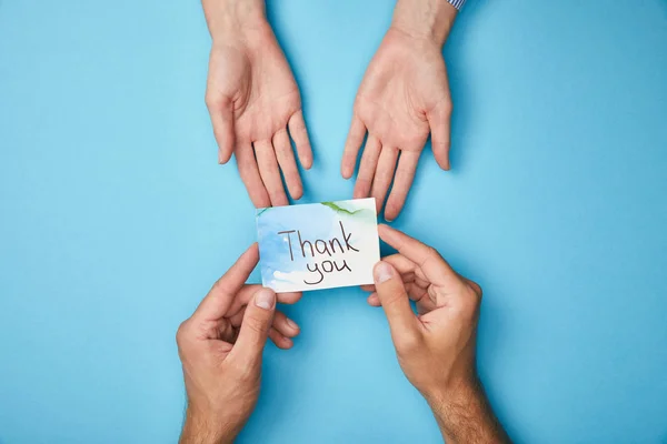 Cropped view of man giving greeting card with thank you lettering to woman on blue background — Stock Photo