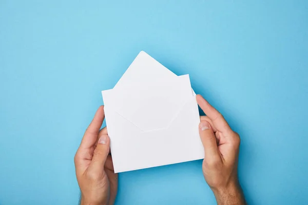 Cropped view of man holding envelope with blank white card on blue background — Stock Photo