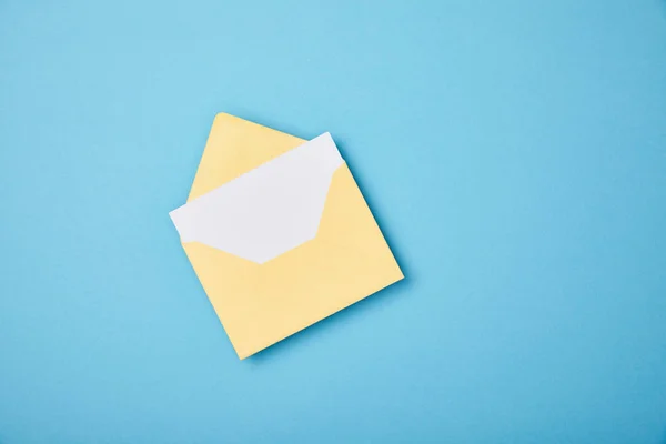 Yellow envelope with blank white card on blue background — Stock Photo