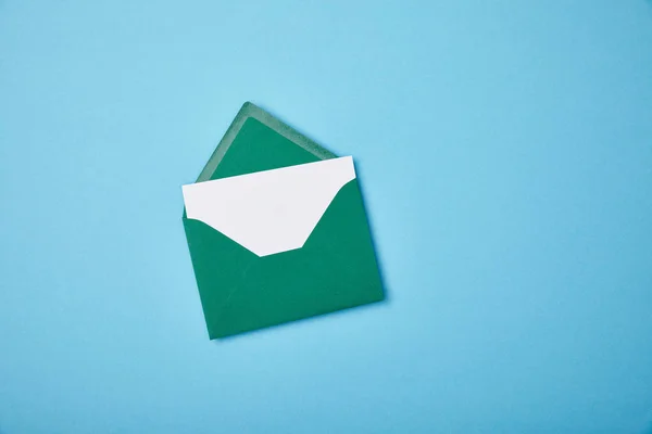 Green envelope with blank white card on blue background — Stock Photo