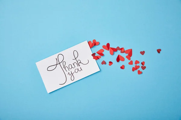Біла листівка з подякою, написи та червоні паперові серця на синьому фоні — стокове фото