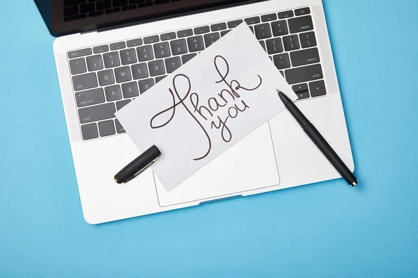 Vista superior do laptop e cartão com letras de agradecimento e caneta no fundo azul — Fotografia de Stock