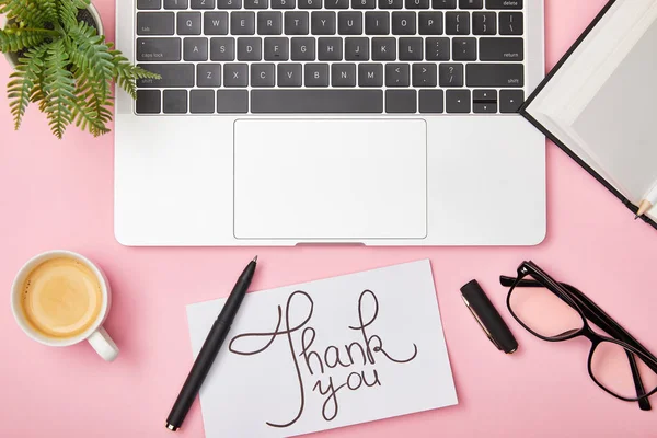 Vista superior de laptop, planta verde, café, notebook, óculos e cartão com obrigado lettering no local de trabalho em fundo rosa — Fotografia de Stock