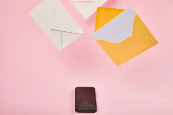 Yellow envelope with blank white card near letters and smartphone with blank screen on pink background — Stock Photo