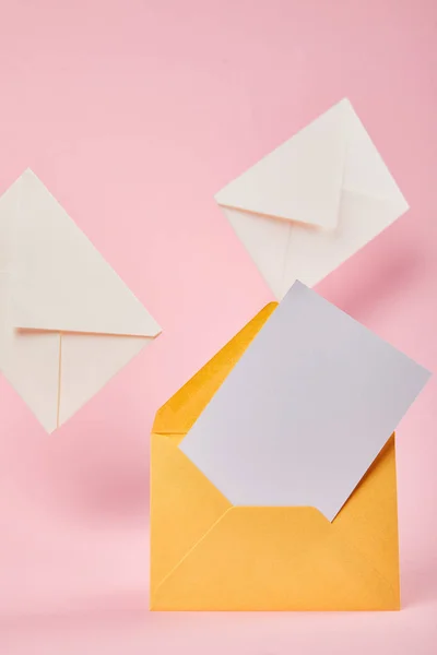 Yellow envelope with blank white card near letters on pink background — Stock Photo