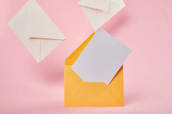 Yellow bright envelope with blank white card near letters on pink background — Stock Photo