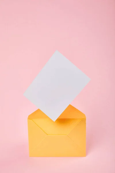 Yellow envelope with blank white card on pink background — Stock Photo