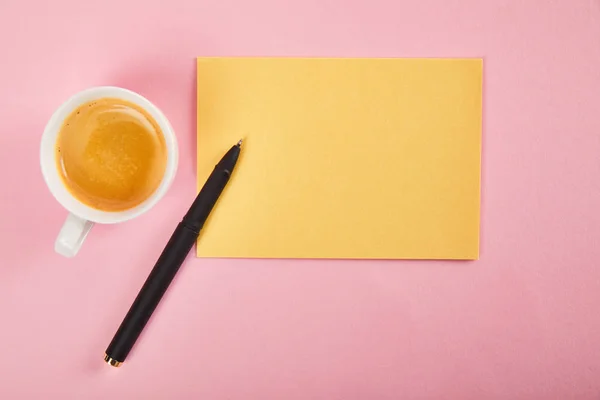 Vista superior do envelope amarelo com caneta e xícara de café no fundo rosa — Fotografia de Stock