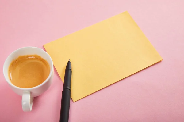 Sobre amarillo con pluma y taza de café sobre fondo rosa - foto de stock