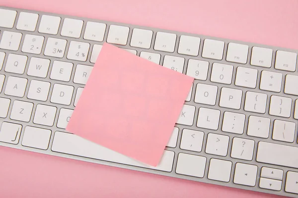 Top view of empty pink sticky note on laptop keyboard on pink background — Stock Photo