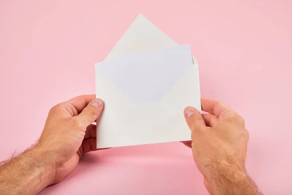 Vista cortada do homem segurando envelope com cartão branco em branco no fundo rosa — Fotografia de Stock