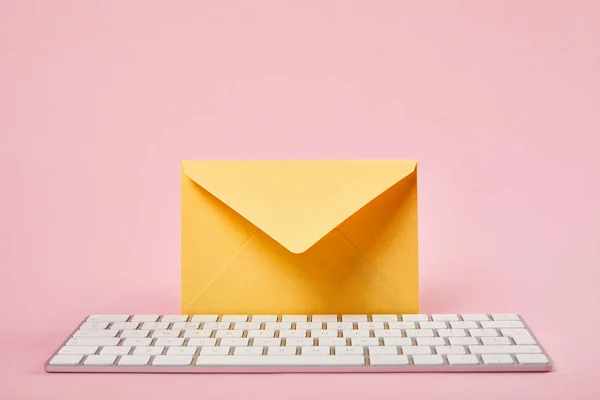 Yellow envelope near white computer keyboard on pink background — Stock Photo