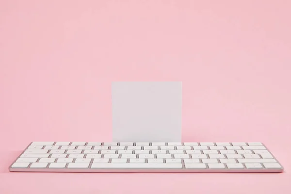 Cartão branco em branco perto do teclado do computador no fundo rosa — Fotografia de Stock