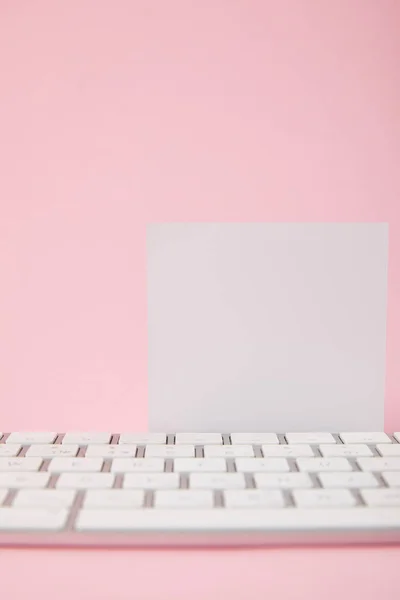 Vista de cerca de la tarjeta blanca en blanco cerca del teclado de la computadora sobre fondo rosa - foto de stock