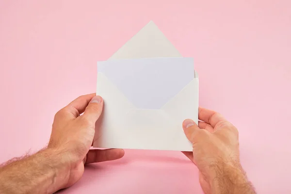 Cropped view of man holding envelope with blank card on pink background — Stock Photo