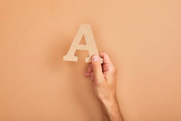 Vista ritagliata di uomo in possesso di carta tagliata lettera A su sfondo beige — Foto stock