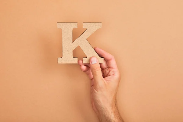 Cropped view of man holding paper cut letter K on beige background — Stock Photo