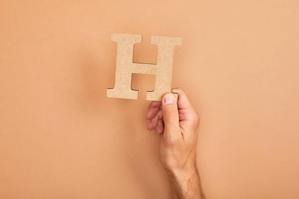 Cropped view of man holding paper cut letter H on beige background — Stock Photo