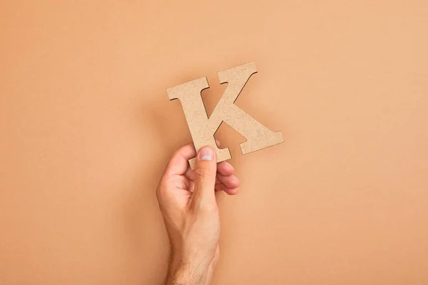 Partial view of man holding paper cut letter K on beige background — Stock Photo