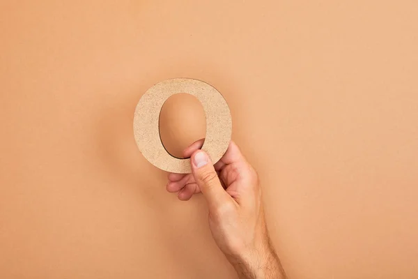 Partial view of man holding paper cut letter O on beige background — Stock Photo