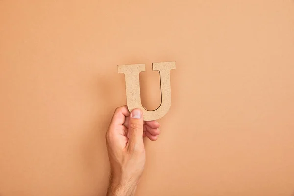 Ausgeschnittene Ansicht einer männlichen Hand, die den Buchstaben u auf beigem Hintergrund hält — Stockfoto