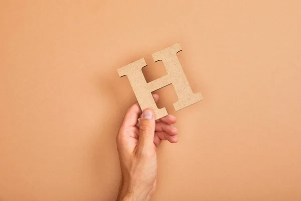Vista parziale dell'uomo in possesso di carta tagliata lettera H su sfondo beige — Foto stock