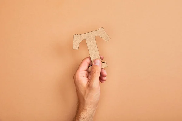 Partial view of man holding paper cut letter T on beige background — Stock Photo