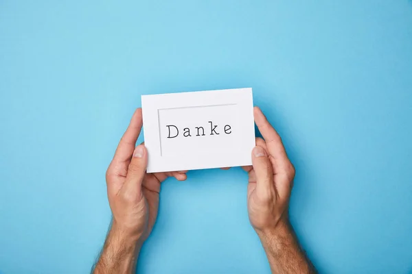 Cropped view of man holding white card in frame with danke word on blue background — Stock Photo