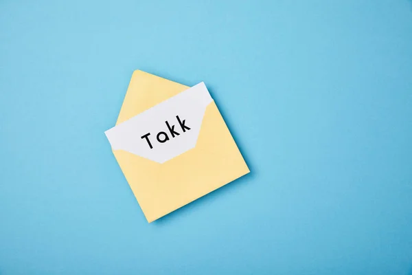 Envelope amarelo e cartão branco com palavra takk no fundo azul — Fotografia de Stock