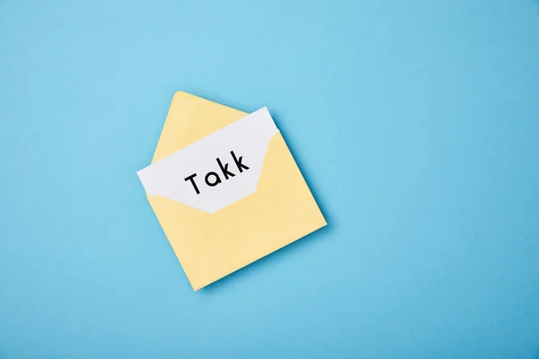 Yellow envelope and white card with takk word on blue background — Stock Photo