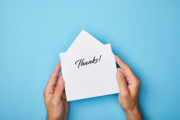 Cropped view of man holding envelope and white card with thanks inscription on blue background — Stock Photo