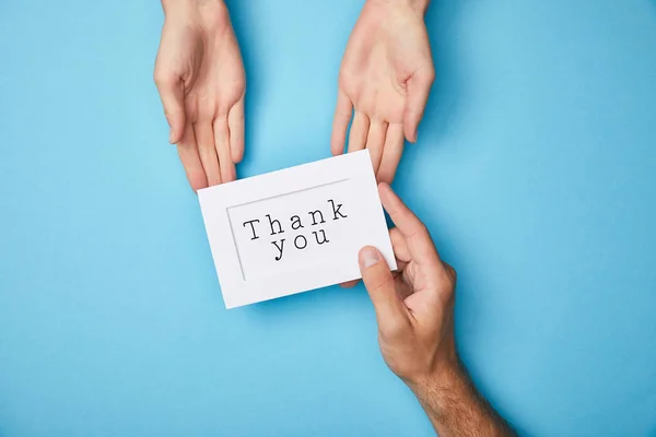 Cropped view of man giving white card in frame with thank you lettering to woman on blue background — Stock Photo