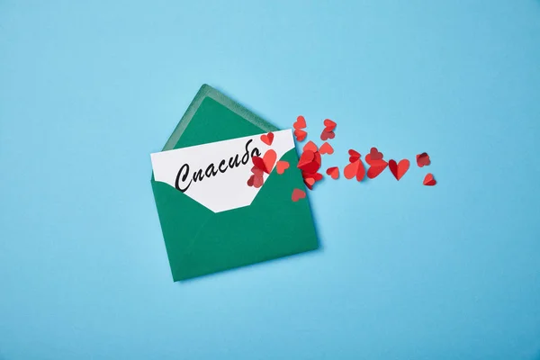 Green envelope with thanks lettering in Russian on white card and red paper hearts on blue background — Stock Photo