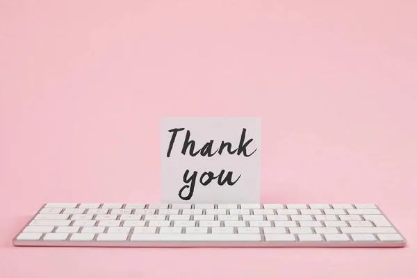 White card with thank you lettering near computer keyboard on pink background — Stock Photo