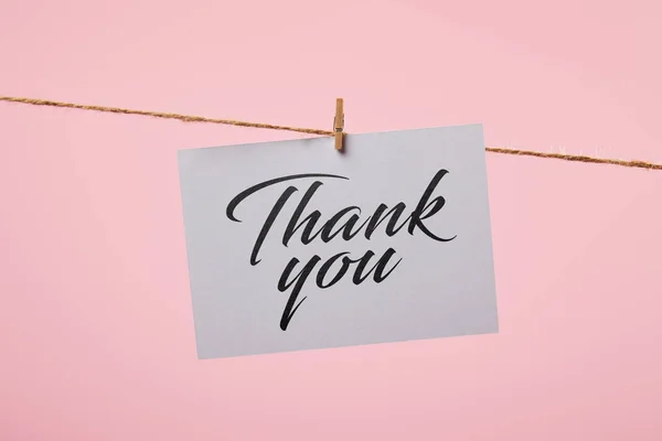 White card with thank you inscription hanging on rope isolated on pink — Stock Photo