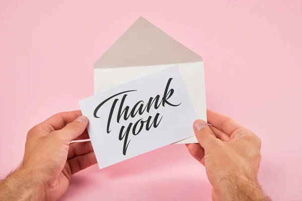 Corte vista de homem segurando envelope com obrigado lettering no cartão branco no fundo rosa — Fotografia de Stock