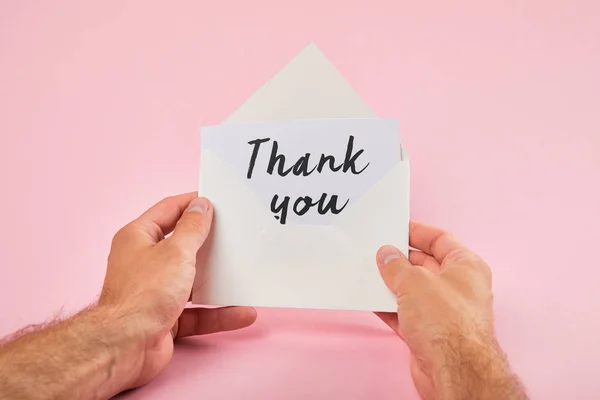 Cropped view of man holding envelope and white card with thank you words on pink background — Stock Photo